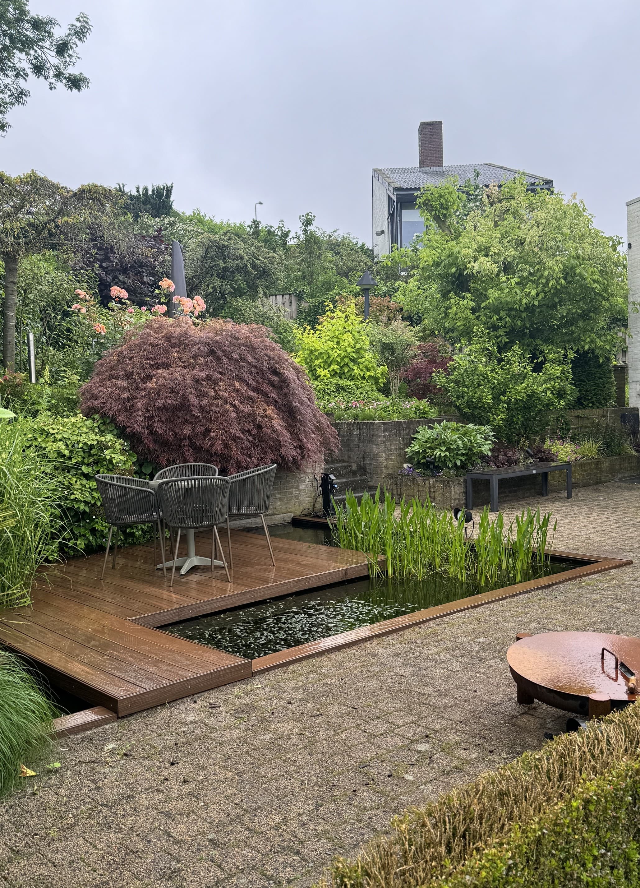 Aangelegde tuin met houten vlonder, vijver en borders
