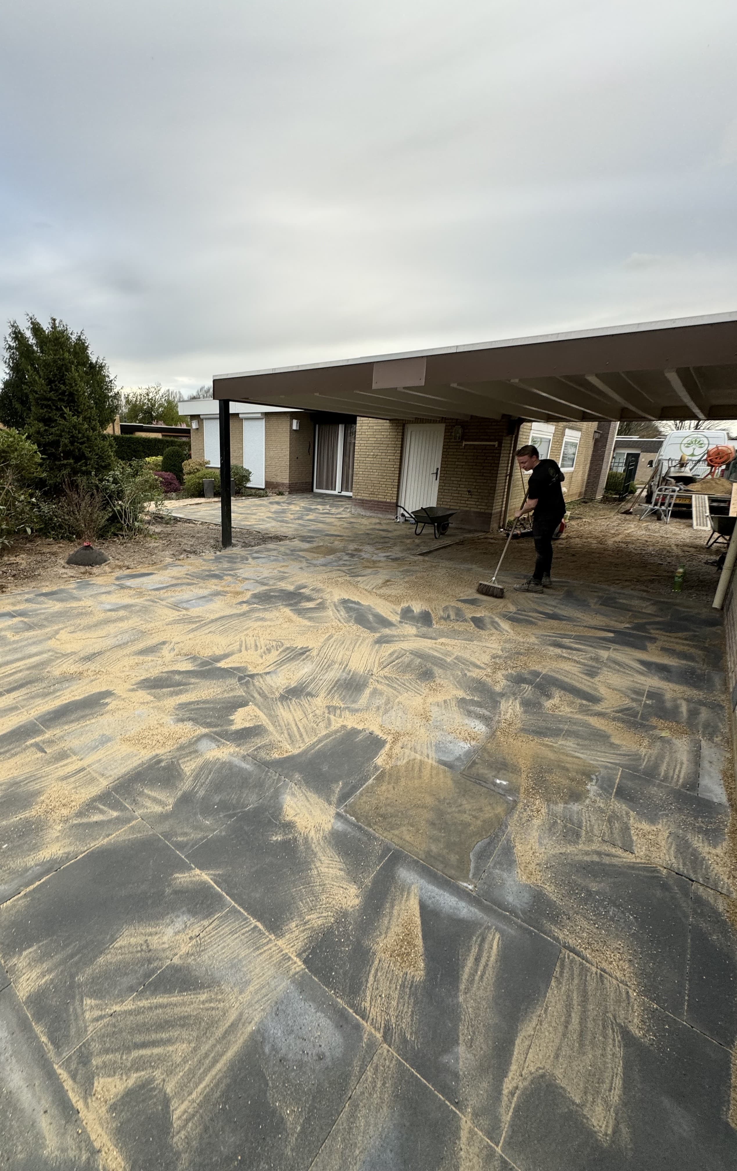 Medewerker van Top Tuinen veegt voegzand in tussen grote terrastegels