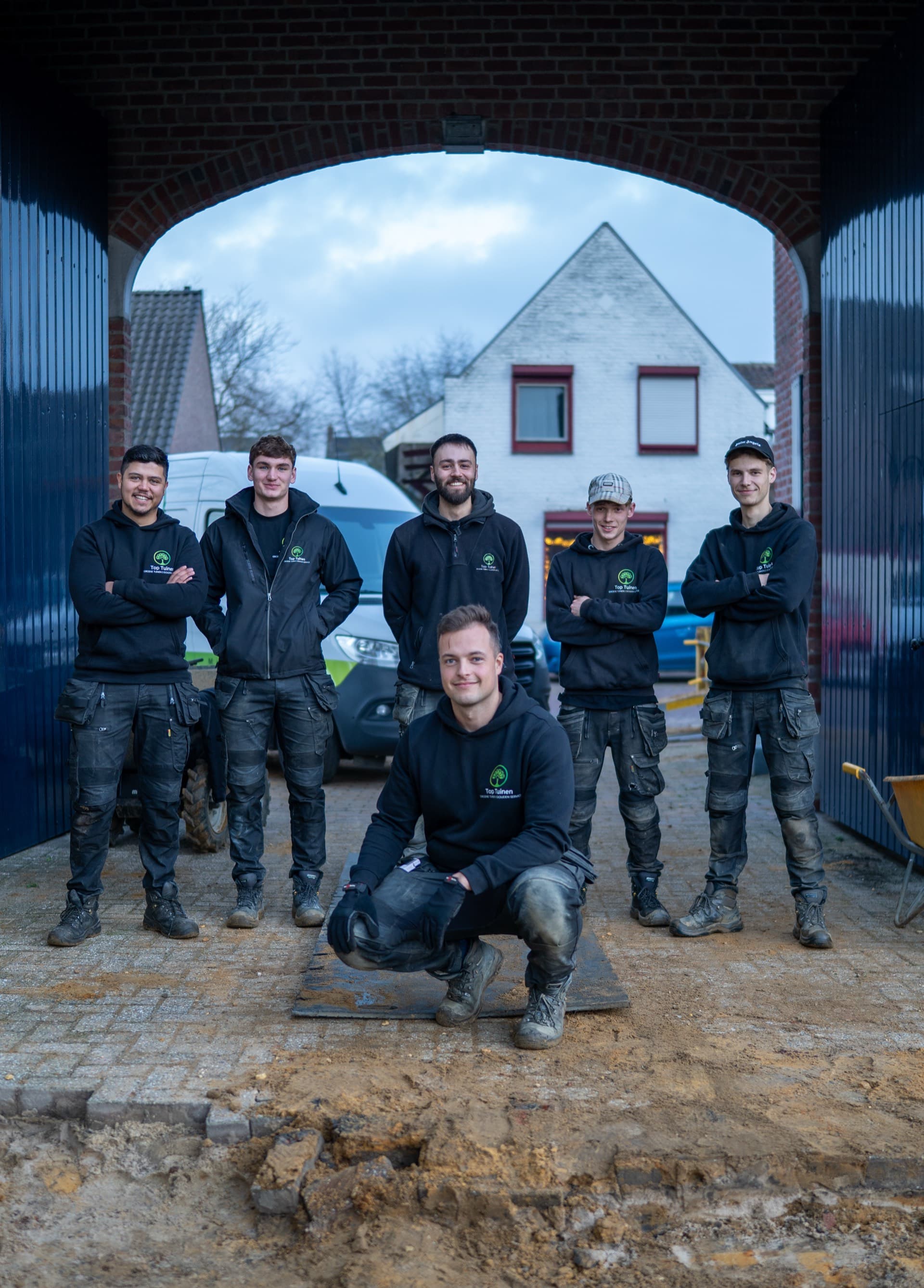 Het team van Top Tuinen voor de poort van de werkplaats